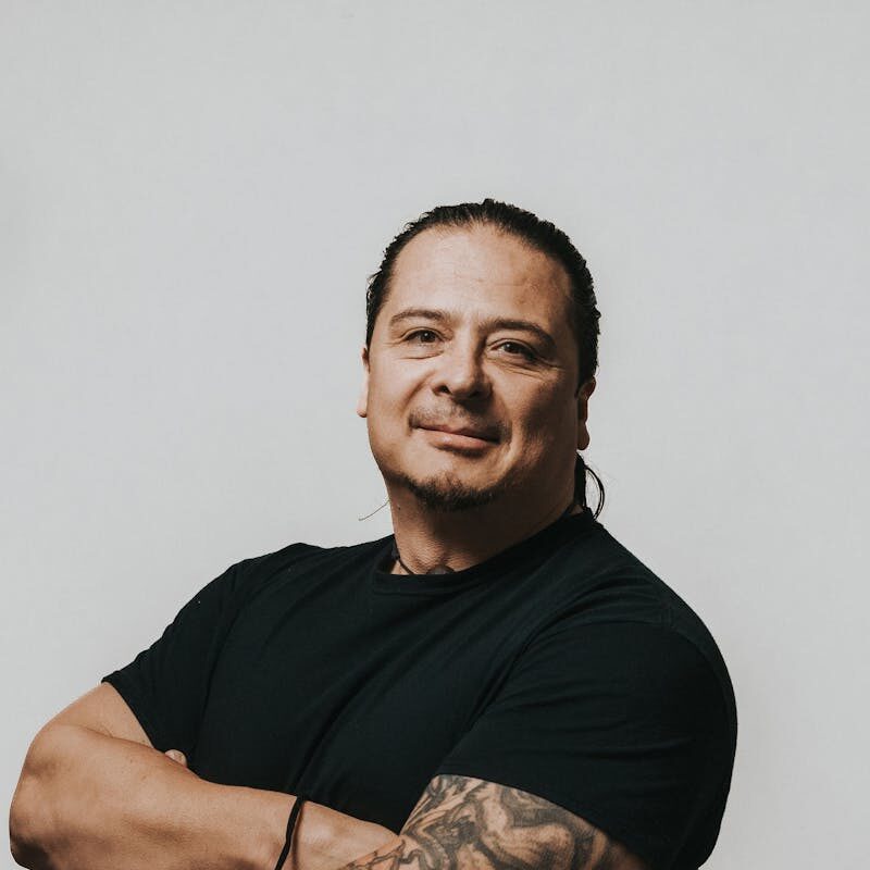 Portrait of a confident man with tattoos, arms crossed and wearing a black t-shirt on a white background.